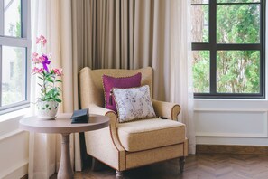 A room with a beige armchair, a small round table with a plant, and a window with a view of trees. - Mercure Dalat Resort (Lam Vien - Da Lat)