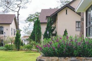 Um edifício residencial com base de pedra, telhado inclinado e um jardim bem cuidado com plantas floridas.