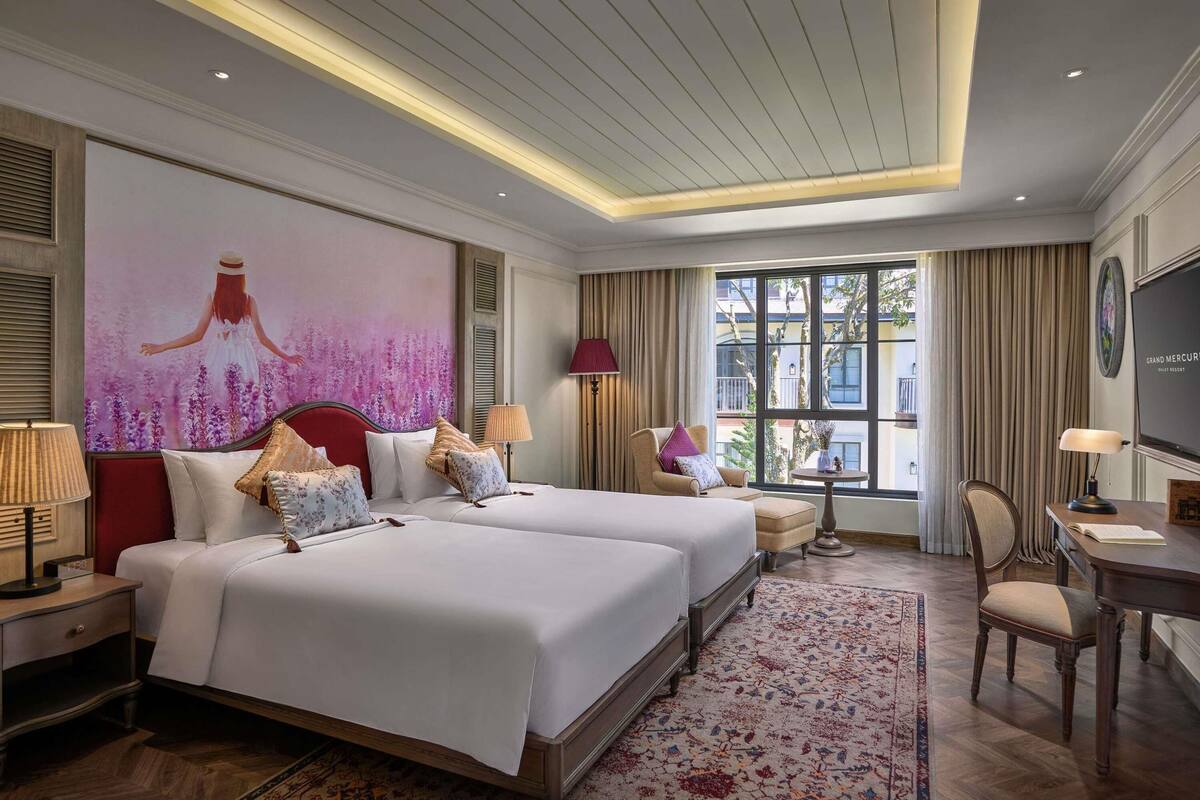 Una habitación de hotel con dos camas, un escritorio, una silla, un televisor y un ventanal con cortinas.