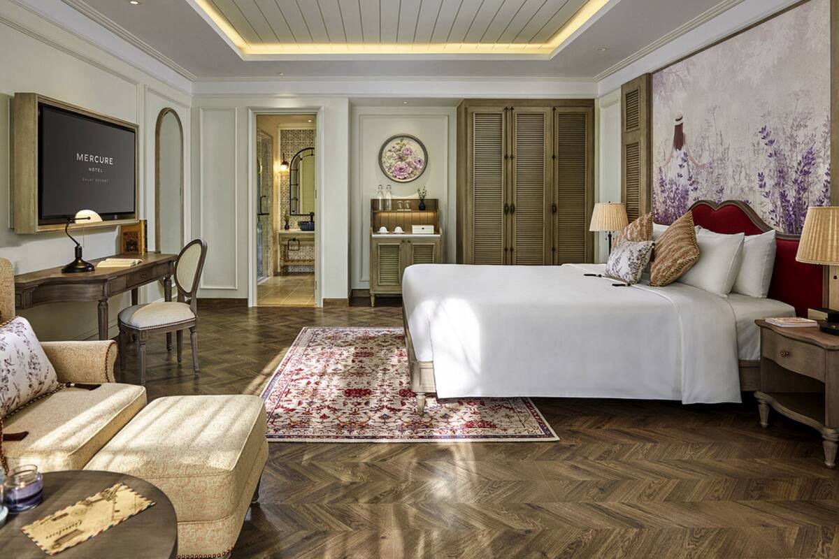 Habitación de hotel con una cama grande, un escritorio, una silla, un televisor, un armario y un cuadro floral grande en la pared.