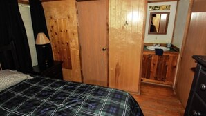 Une chambre à coucher aux murs lambrissés, comprenant un lit, une table de chevet, une commode et une salle de bain avec un lavabo et un miroir.
