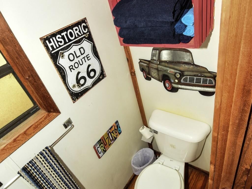 Ein Badezimmer mit Toilette, Waschbecken und Spiegel. An der Wand befindet sich ein Schild mit der Aufschrift "Historic Old Route 66".