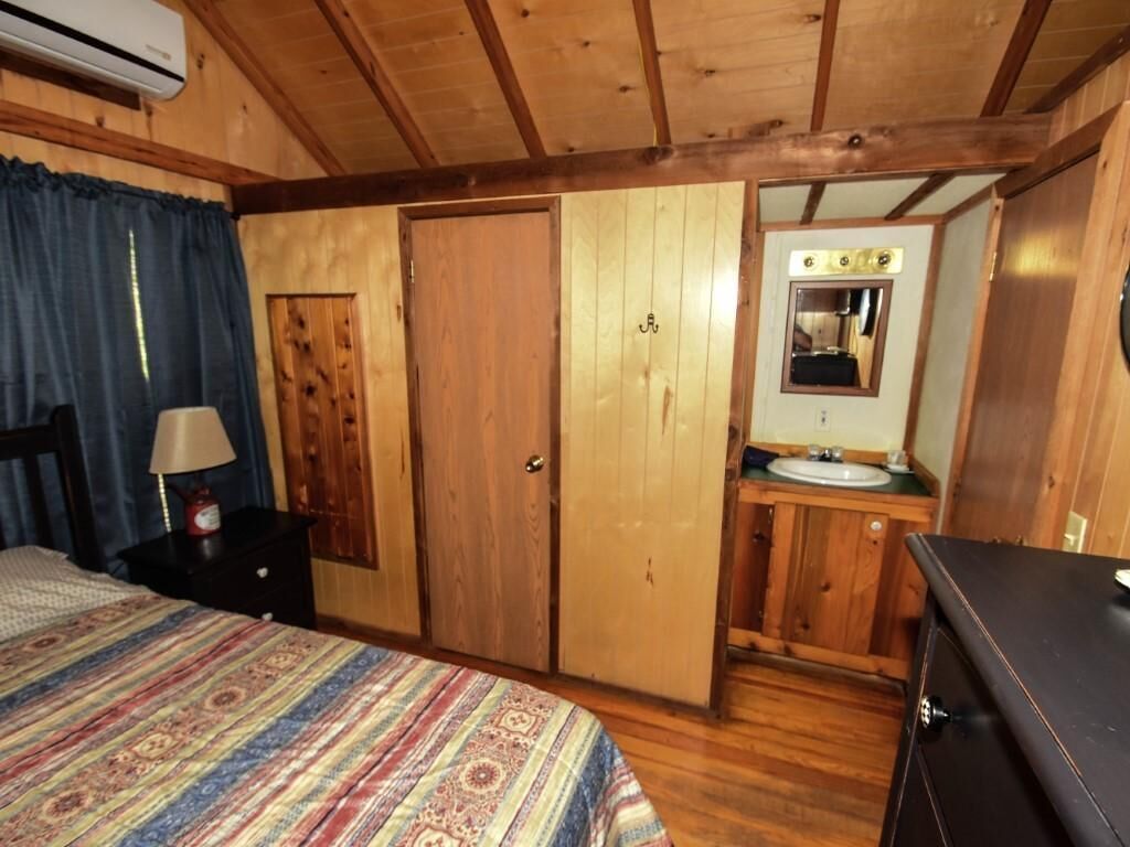 Ein Zimmer in einer Holzhütte mit einem Bett, einem Schminktisch, einem Spiegel und einem kleinen Badezimmer.