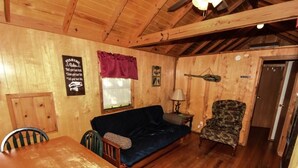 A wooden cabin interior with a dining table, two chairs, a blue sofa, a patterned armchair, and a wooden ceiling with exposed beams. - Lake Texoma Cedar Cabin - Striper King (Mead)