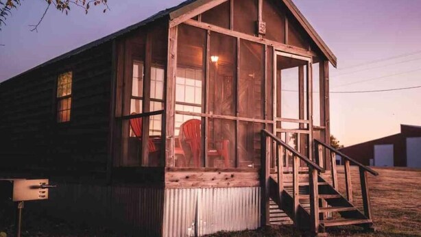 A wooden cabin with a porch, large windows, and a staircase leading to the entrance. - Lake Texoma Cedar Cabin - Striper King (Mead)
