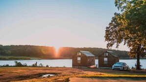 Two wooden cabins by a lake with a car parked in front. - Lake Texoma Cedar Cabin (Mead)