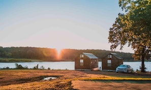 Dos cabañas de madera junto a un lago, con un coche estacionado adelante.