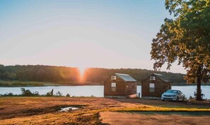 Two wooden cabins by a lake with a car parked in front. - Lake Texoma Cedar Cabin (Mead)