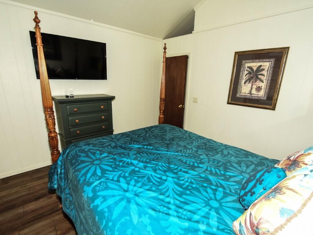 Une chambre à coucher avec un lit à baldaquin, une commode, un téléviseur fixé au mur et un tableau encadré.