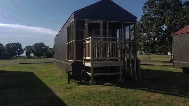 A wooden structure with a porch, a small table, and a chair. - Lake Texoma Lakefront Cabin - Texoma Breeze (Mead)