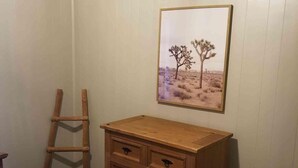 Ein Schlafzimmer mit einem hölzernen Schminktisch, einer Stehleiter und einem gerahmten Bild einer Wüstenlandschaft.