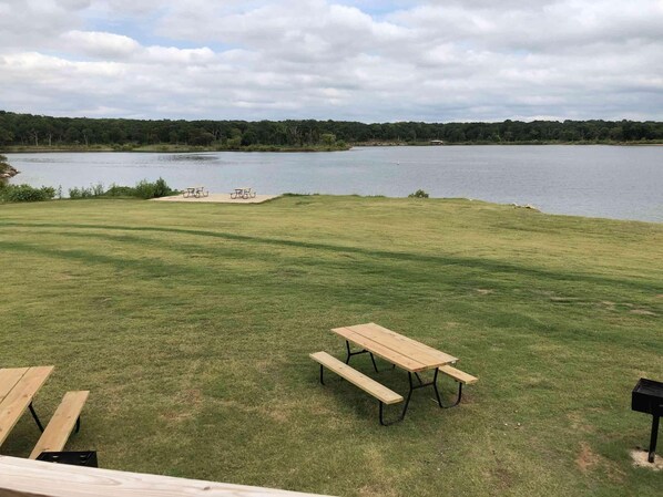 Une zone herbeuse avec des tables de pique-nique et un lac en arrière-plan.