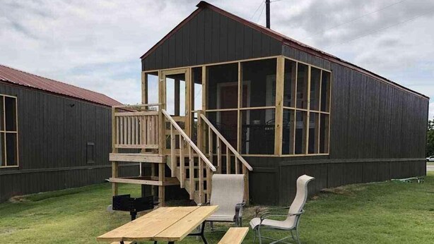 A wooden deck with a picnic table and chairs, a small staircase, and a building with large windows and a dark exterior.