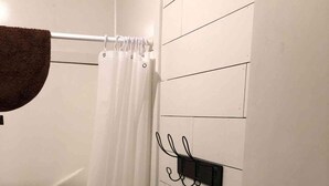 A bathroom with a white tiled wall, a shower curtain, a towel rack, and a door with a brass handle.
