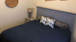 A bedroom with a bed, a bedside table with a lamp, a wall-mounted paddle, and a round woven item.