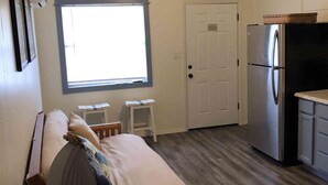 A compact kitchen with a refrigerator, a wooden dining table, and a ceiling fan.
