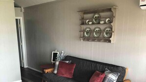 A living room with a dark grey sofa, a wooden bench, and a white chair. There is a wall-mounted shelf with decorative plates.