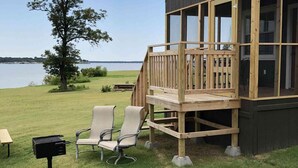 A wooden deck with two chairs and a grill, overlooking a lake.