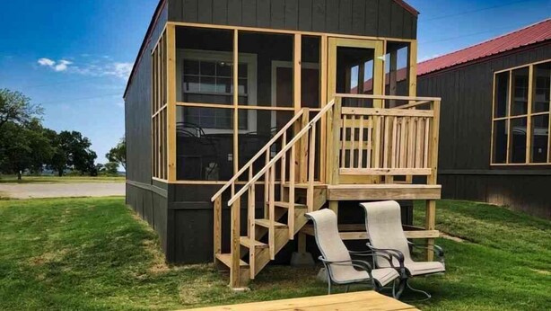 A small, dark-colored wooden structure with a balcony and a staircase leading to a deck area.