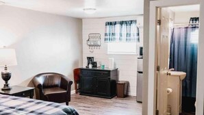A hotel room with a bed, a desk, a chair, a cabinet, and a bathroom with a sink and shower curtain. - Lake Texoma Quad-plex (Mead)