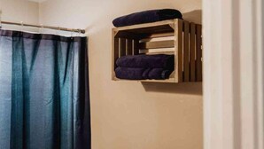 A bathroom with a shower curtain and a wooden shelf with towels. - Lake Texoma Quad-plex (Mead)
