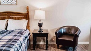 A bedroom with a wooden headboard bed, a bedside table with a lamp, and a leather armchair. - Lake Texoma Quad-plex (Mead)