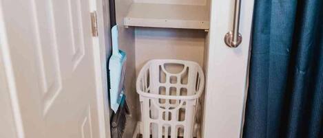 A laundry basket in a bathroom with a shower curtain and a towel rack.