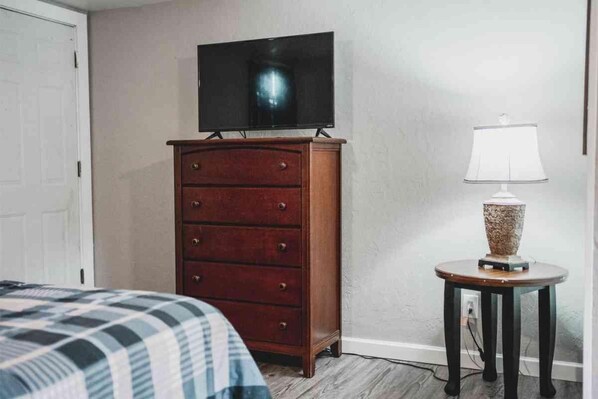 Un dormitorio con un aparador de madera, un televisor encima, una lámpara de noche y una cama con una colcha a cuadros.