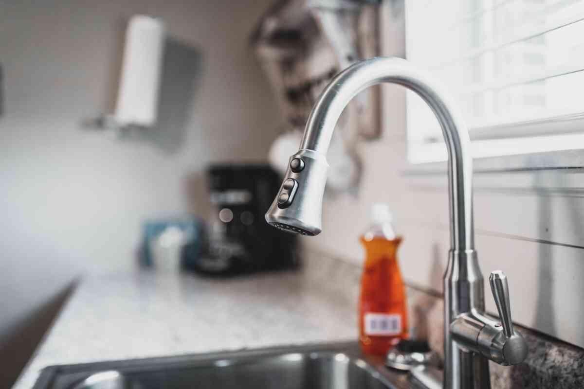 Een keuken met een moderne kraan, een koffiezetapparaat en een fles afwasmiddel op het aanrecht.