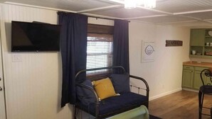 A room with a bed, a television mounted on the wall, a window with curtains, and a kitchenette area.