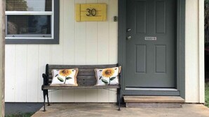 A front porch with a bench, a door, and a number sign.