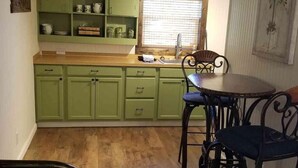 A kitchen with green cabinets, a wooden countertop, a sink, and a dining table with chairs.