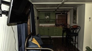 A compact living space with a metal-framed couch, a dining table with chairs, and a kitchenette with green cabinets.