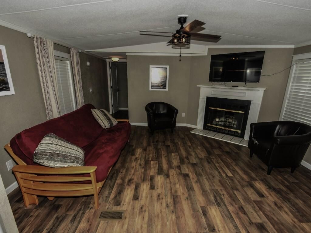 Un salon avec un canapé rouge, un fauteuil noir, une cheminée et un ventilateur de plafond.