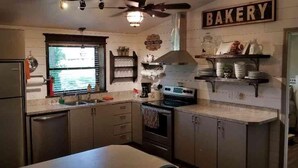A kitchen with stainless steel appliances, a window with blinds, and a 'BAKERY' sign on the wall. - Lake Texoma Lakeside Cottage (Mead)