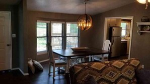 A compact kitchen with a dining table and chairs, a hanging light fixture, and a view of the outdoors through the windows. - Lake Texoma Lakeside Cottage (Mead)