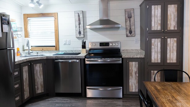 Una cocina con refrigerador de acero inoxidable, lavavajillas, horno y una mesa de madera.