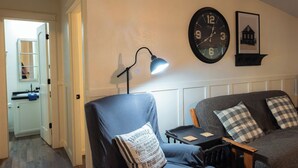 A living room with a sofa, a chair, a clock, a lamp, and a framed picture on the wall. - Lake Texoma Vacation Home The Farm House (Mead)