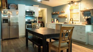 Uma cozinha moderna com mesa de jantar, cadeiras, geladeira, micro-ondas, forno e ventilador de teto.