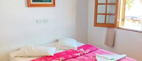 A single bed with a red floral bedspread, a white pillow, and a framed picture on the wall.