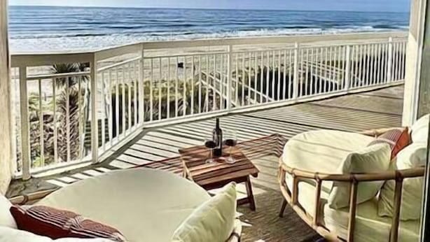 Ein Balkon mit Blick auf den Ozean, eine Holzterrasse und Gartenmöbel.
