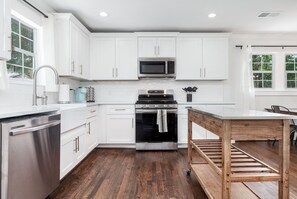 Een moderne keuken met witte kastjes, roestvrijstalen apparatuur en een houten tafel.