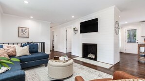 A modern living room with a blue sofa, a fireplace, and a flat-screen TV mounted above it. - Crestwood Contemporary - Minutes to Downtown! (Birmingham)