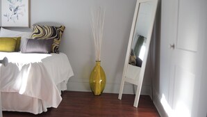 A bedroom with a bed, pillows, a vase, a mirror, and a door.