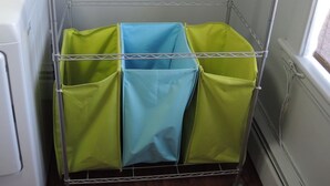 A laundry area with a metal rack holding green and blue laundry bags, a white washing machine, and a window with a view of the outside.