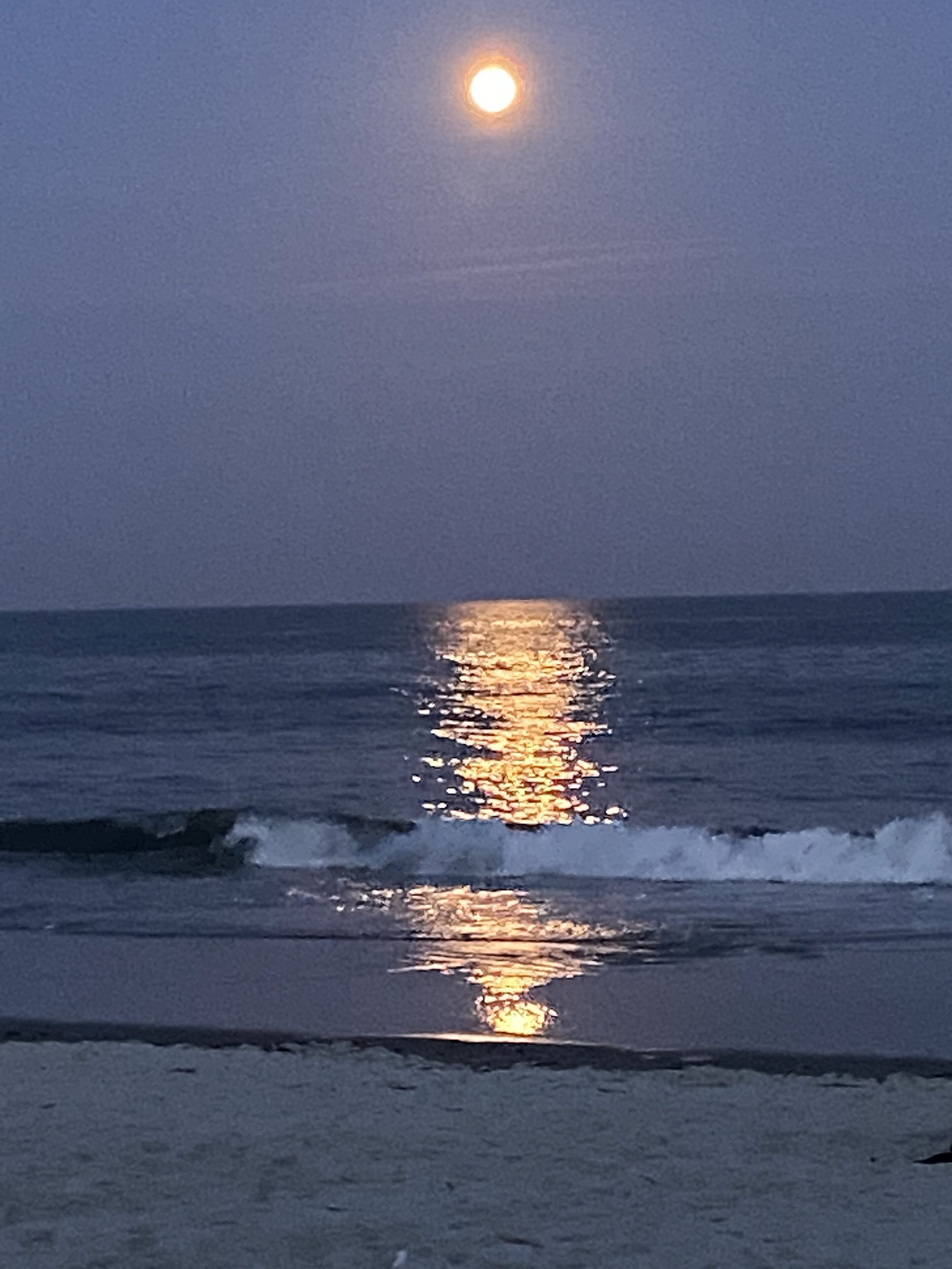 A beach scene with the moon reflecting on the water.