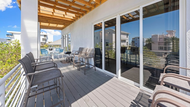 Una terraza cubierta al aire libre con suelo de madera, mobiliario exterior y grandes puertas correderas de cristal que dan a un balcón.