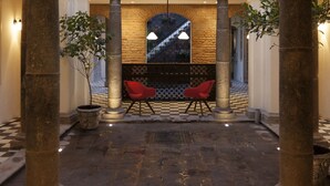 Un lobby espacioso con piso a cuadros, una escalera central y sillones rojos.