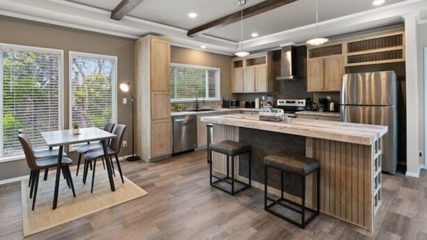 A modern kitchen with a central island, wooden cabinets, stainless steel appliances, and a dining area with a table and chairs. - 8 acres Ranch - 2 Homes - Sleeps 16 - Dripping (Dripping Springs)