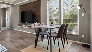 A modern living room with a dining area, a flat-screen TV, and large windows with blinds. - 8 acres Ranch - 2 Homes - Sleeps 16 - Dripping (Dripping Springs)